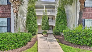 A two-story building with a central courtyard, surrounded by well-maintained hedges and palm trees.