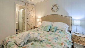 A bedroom with a bed, a nightstand, a wall-mounted lamp, a wooden door, and a shower area.