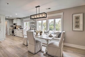 A modern kitchen with white cabinetry, a dining area with a white table and chairs, and large windows offering a view of the outdoors. - Pet-friendly Villa w/ Balcony in Bluffton! (Bluffton)