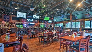 Un restaurant doté de nombreuses tables et chaises, de téléviseurs fixés au plafond et d’un bar avec diverses bouteilles et décorations.
