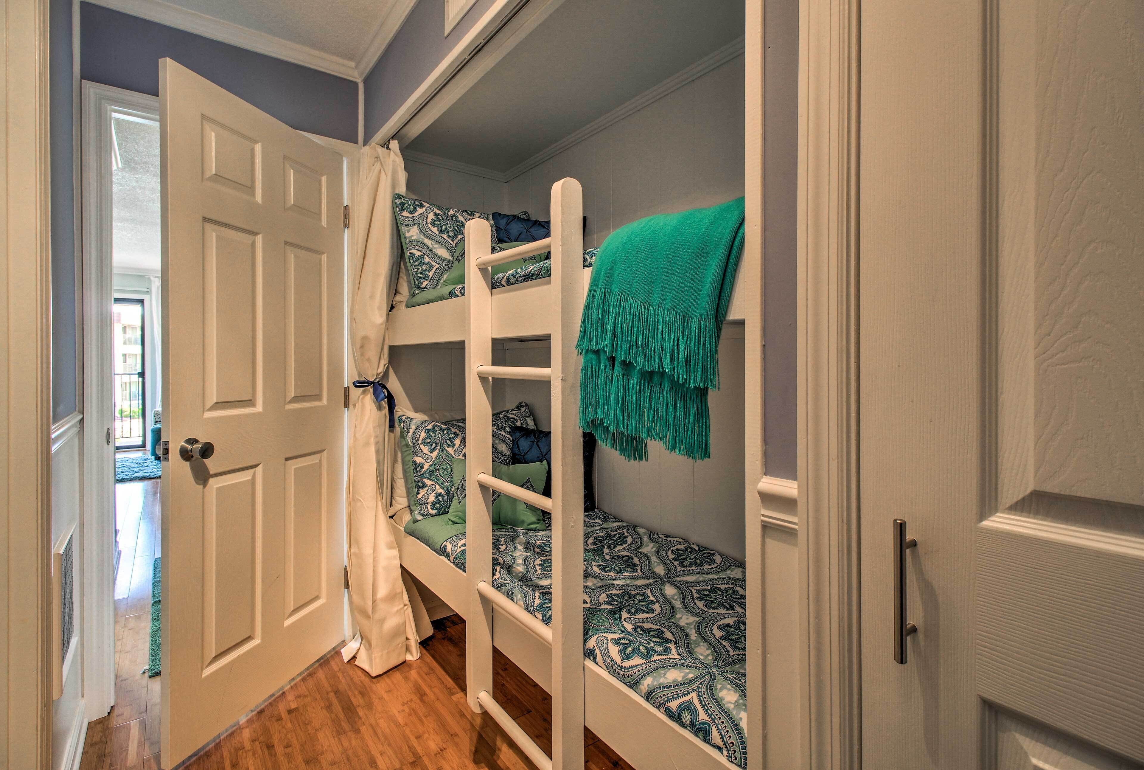 A room with a bunk bed, a white door, and a view of the outside.