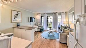Une cuisine moderne avec un coin repas, un salon doté d’un canapé et d’une table basse, et un balcon avec des rideaux.