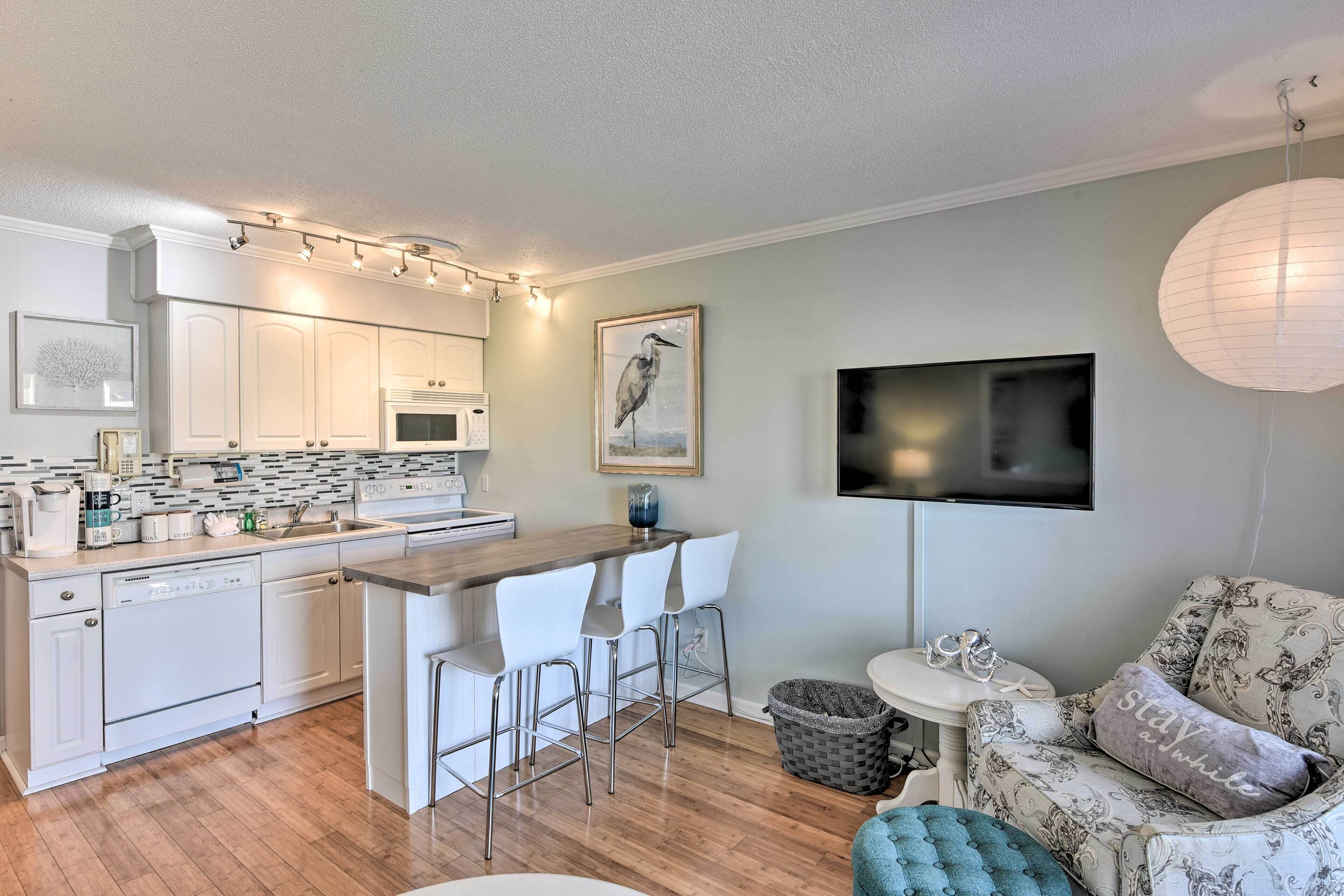 A modern kitchen with white cabinets, a bar area, and a seating space with a patterned sofa and a TV mounted on the wall.