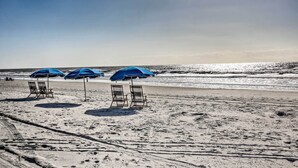 Une plage avec trois parasols bleus et deux chaises en bois.
