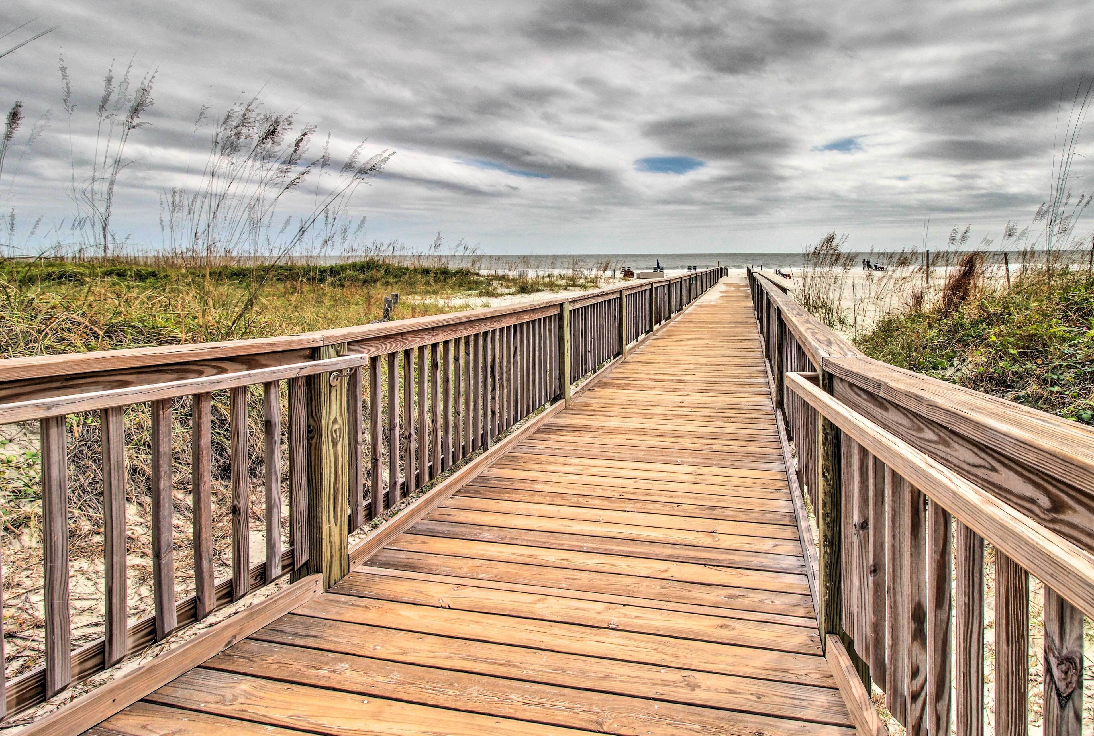 Une promenade en bois menant à une plage, avec un ciel nuageux.