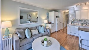 Un salon moderne avec un canapé gris, une table basse ronde ornée d’une plante et un grand miroir placé au-dessus du canapé.