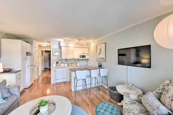A modern kitchen with white cabinets, a central island with bar stools, and a flat-screen TV mounted on the wall. - Beach & Pool Access: Hilton Head Condo w/ Balcony (Hilton Head Island)
