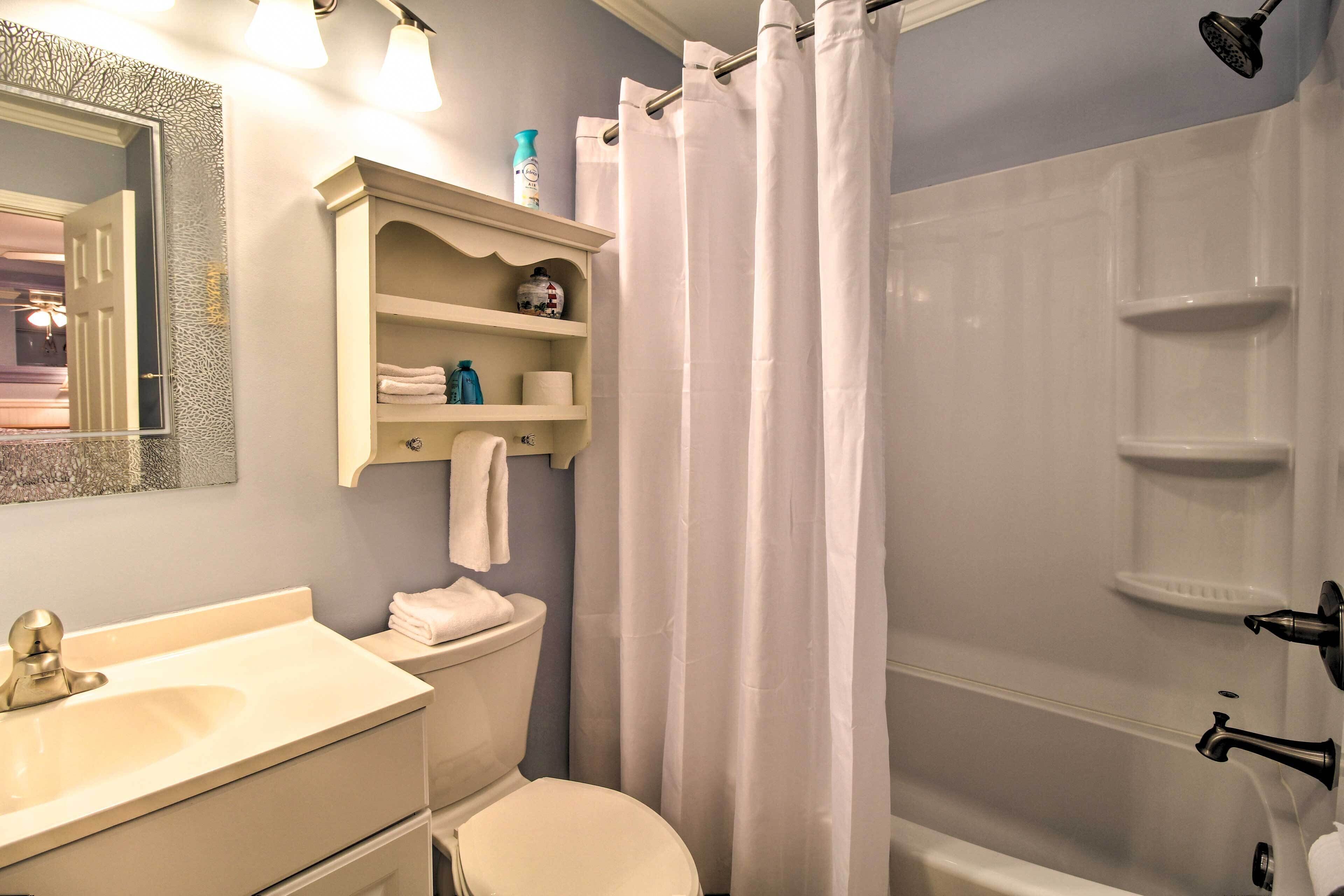 A bathroom with a sink, toilet, and shower area. There is a shelf with toiletries and a towel rack.