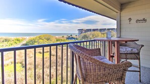 A balcony with wicker chairs and a table, overlooking a beach and a building in the distance. - Beach View, Pool & Tennis: Hilton Head Island Unit (Hilton Head Island)