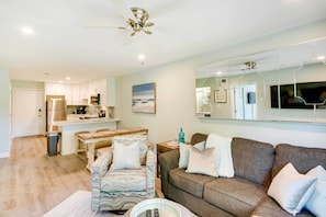 Uma sala de estar moderna com um sofá, uma poltrona estampada e um espaço de jantar com mesa e cadeiras.