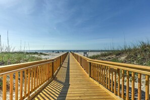 Une promenade en bois qui mène à une plage bordée de dunes de sable et d’une végétation clairsemée.