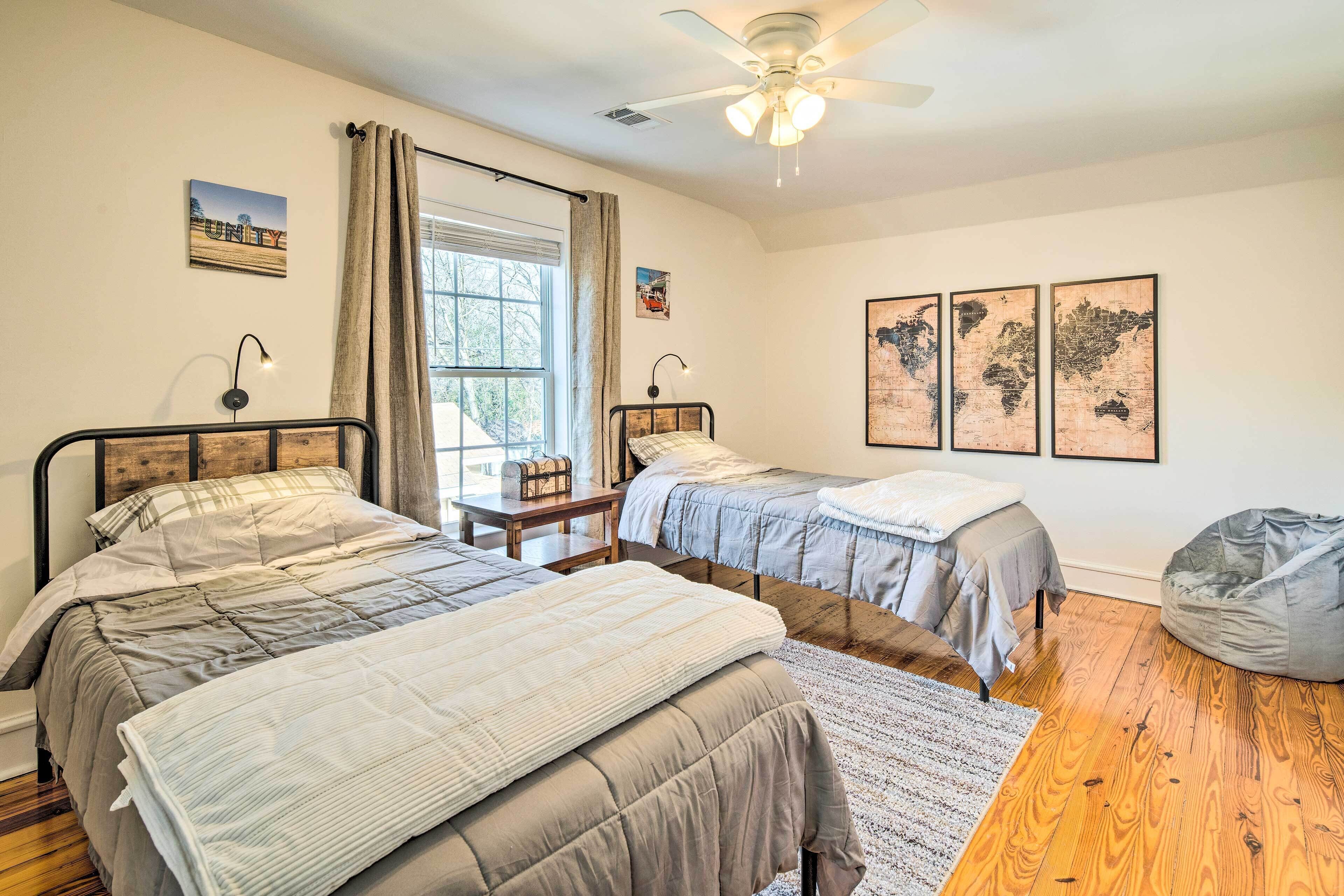 Un dormitorio con dos camas, ventilador de techo, ventana con cortinas y decoración en la pared.
