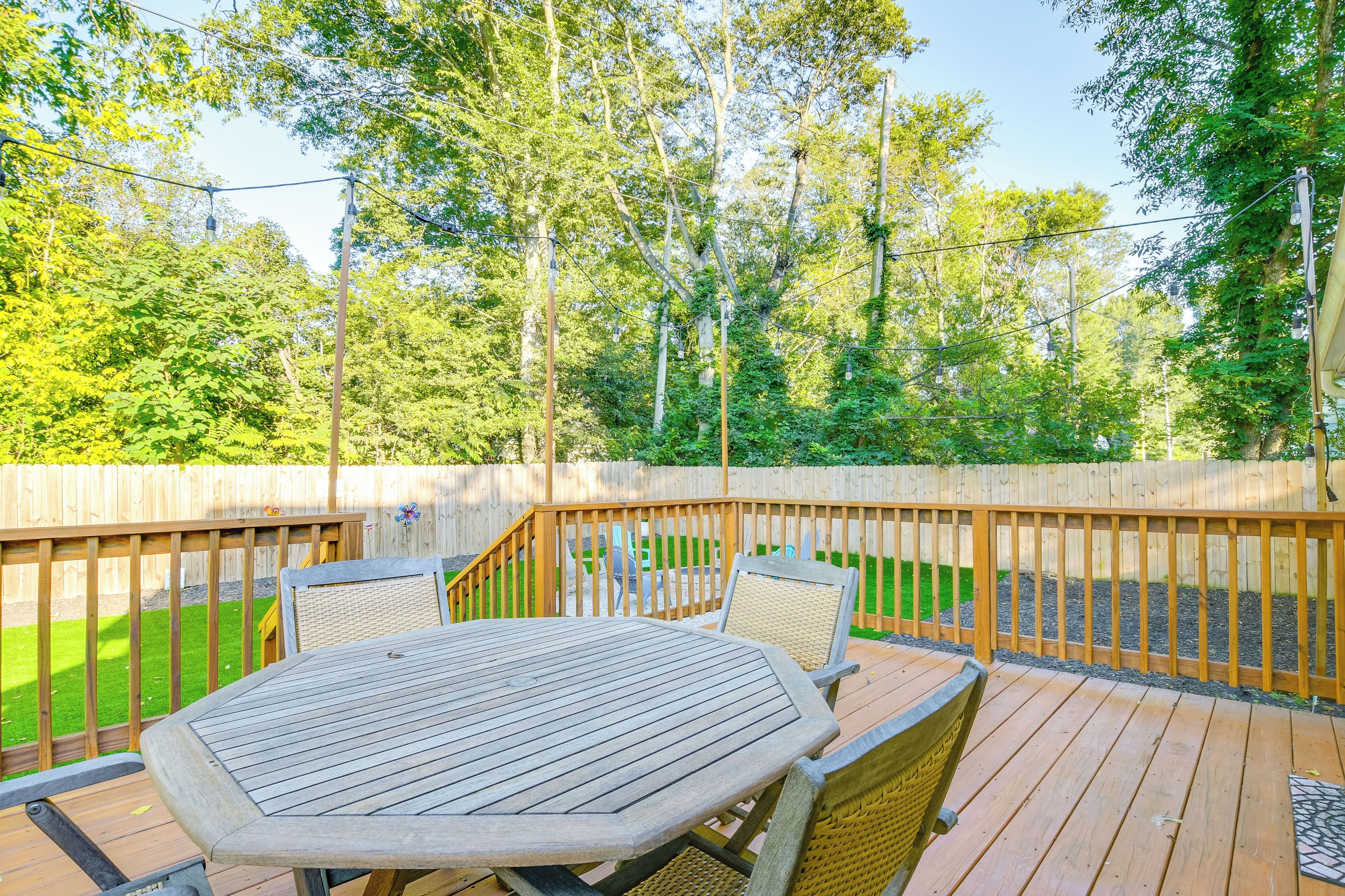 A wooden deck with a round table and chairs, surrounded by a wooden fence and trees.
