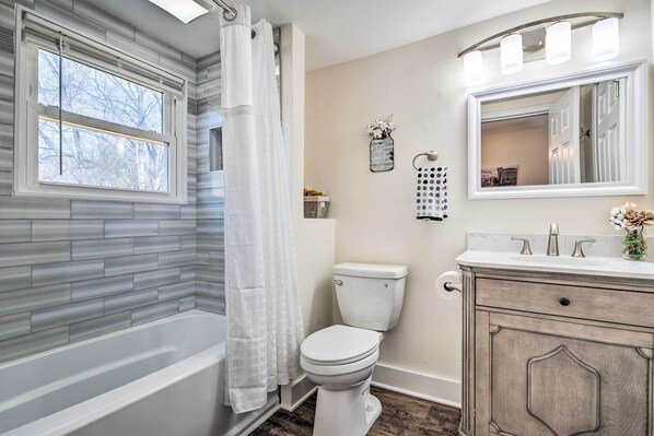 A bathroom with a bathtub, toilet, vanity, and a large mirror.