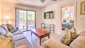 A living room with a sofa, a coffee table, a TV, and a ceiling fan. - Hilton Head Condo: Pool, Hot Tub & Tennis Access! (Hilton Head Island)