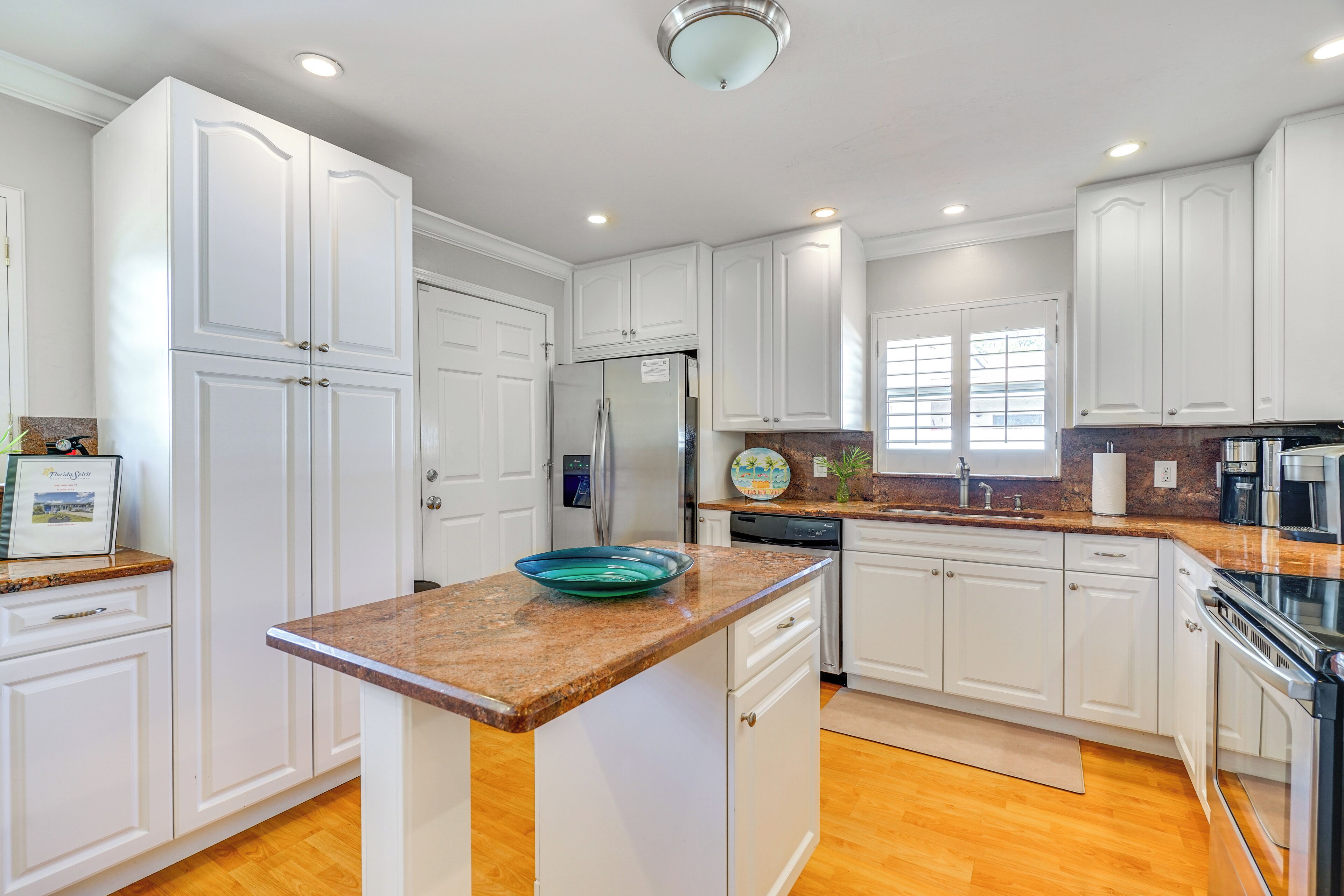A modern kitchen with white cabinetry, granite countertops, a stainless steel refrigerator, and a built-in oven.