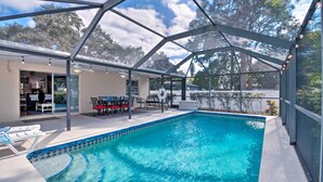 A covered swimming pool with lounge chairs, a dining area, and a view of the surrounding trees. - Breezy Sarasota Home w/ Private Pool Near Beach! (Sarasota)