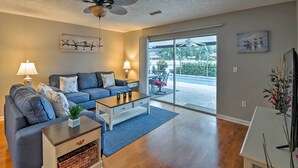 A living room with a sofa, coffee table, and a ceiling fan. There is a sliding glass door leading to an outdoor area with a patio table and chairs. - Breezy Sarasota Home w/ Private Pool Near Beach! (Sarasota)
