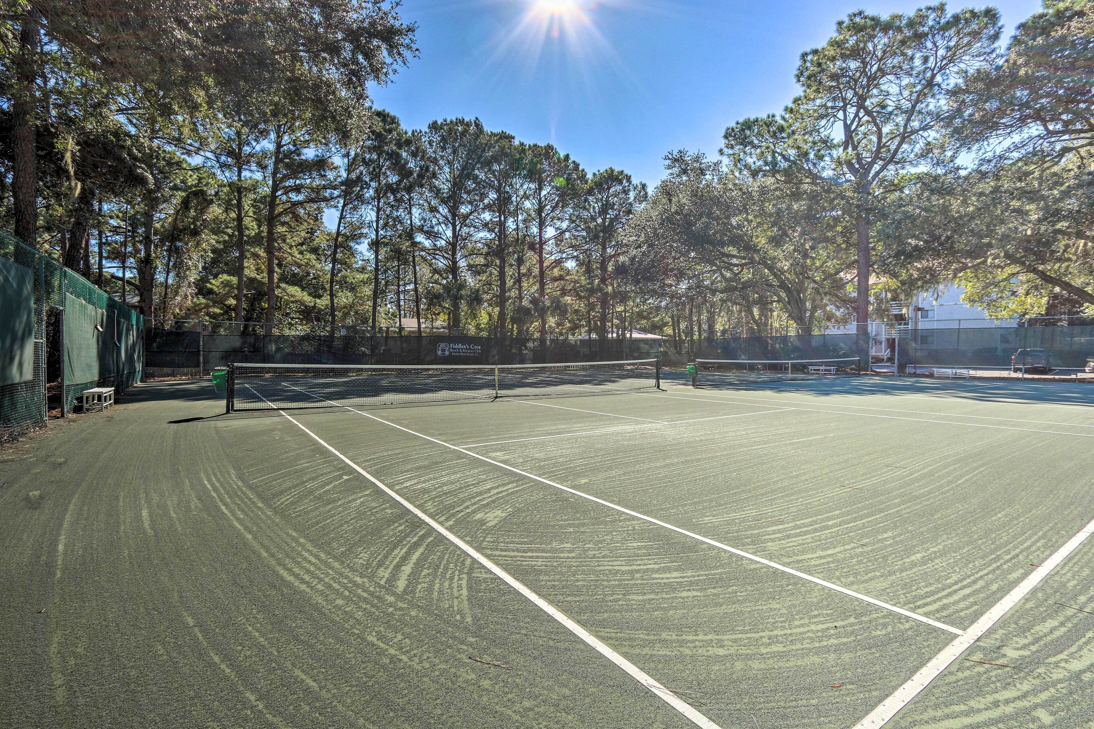 Cancha de tenis con red, rodeada de árboles y una valla.