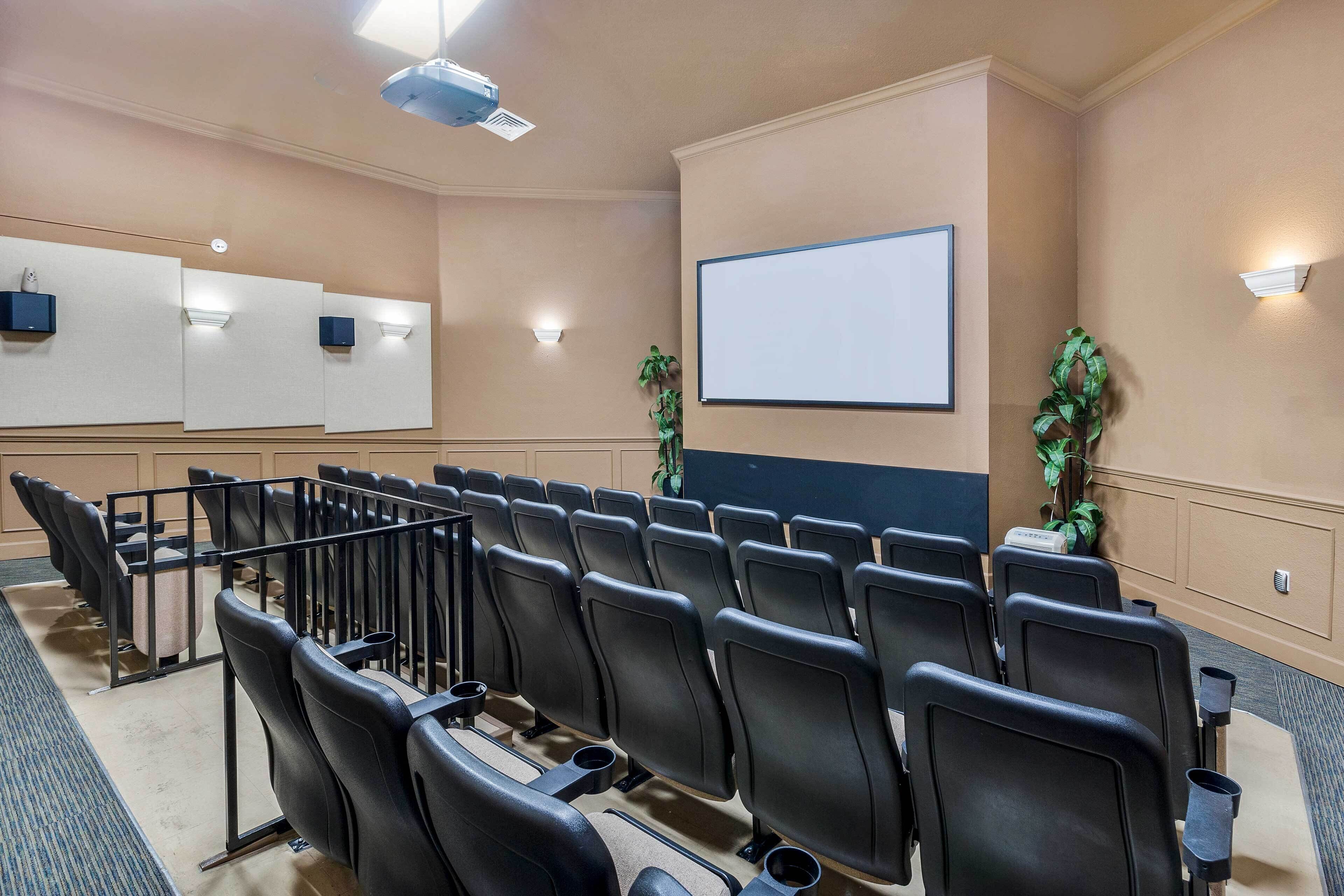 A conference room with rows of black chairs, a large projection screen, and a podium.