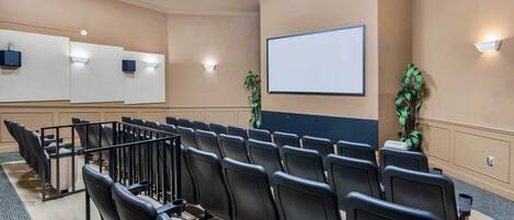 A conference room with rows of black chairs, a large projection screen, and a podium.