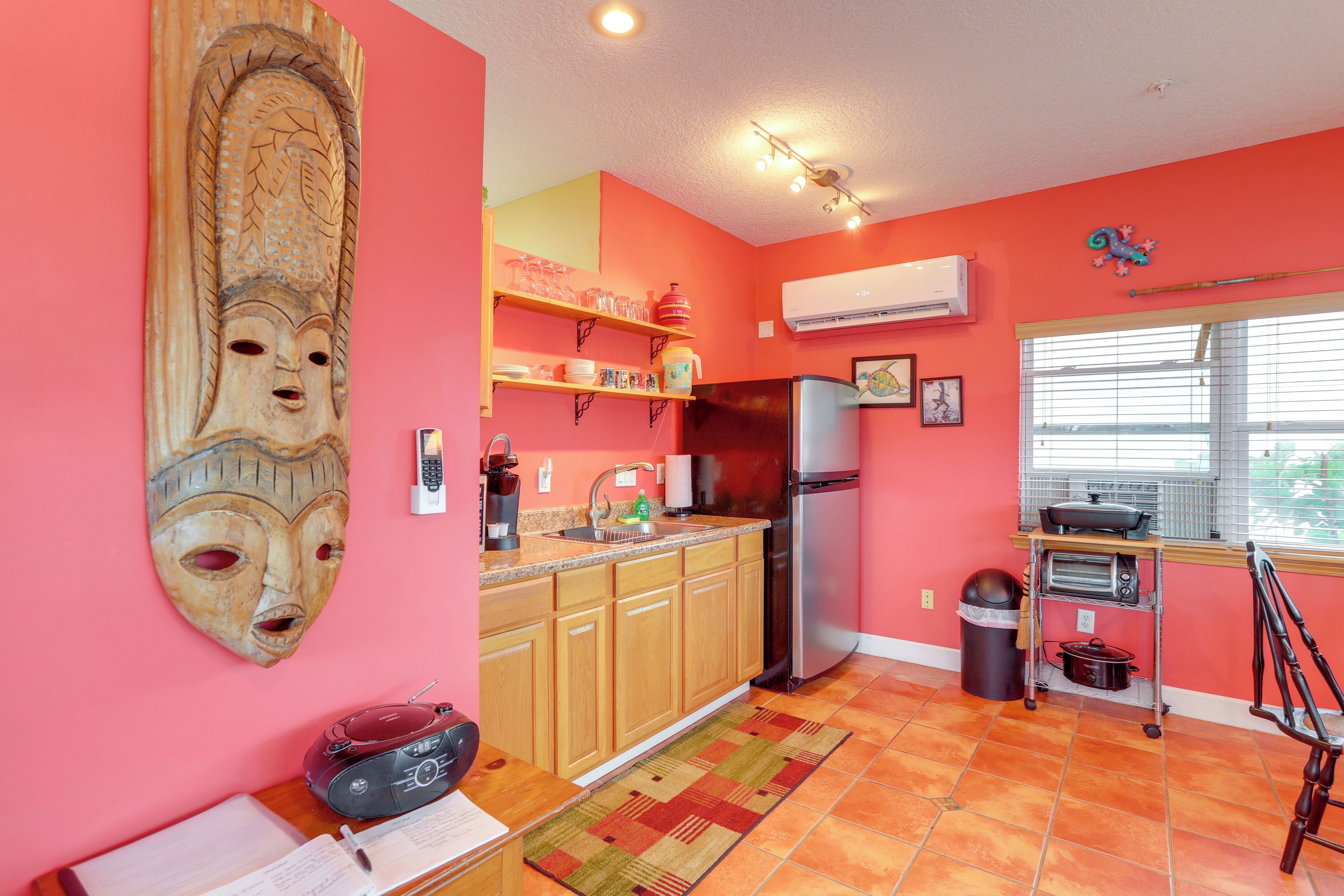 A kitchen with wooden cabinets, a refrigerator, a microwave, and a window with blinds.