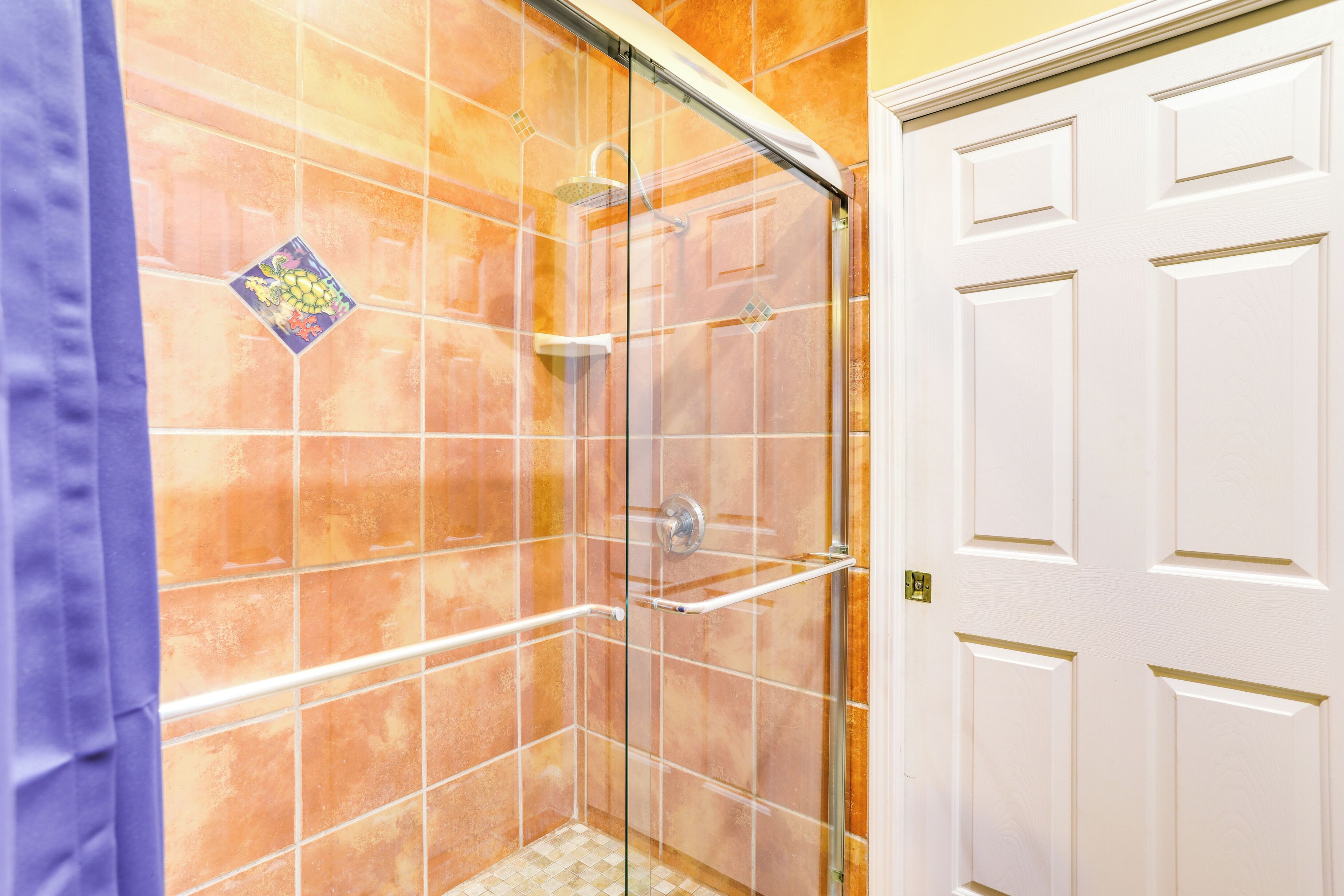 A bathroom with a glass shower enclosure, a white door, and a tiled wall.
