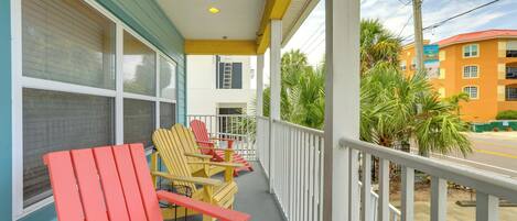 A balcony with red and yellow Adirondack chairs, a small table, and a view of a building across the street.