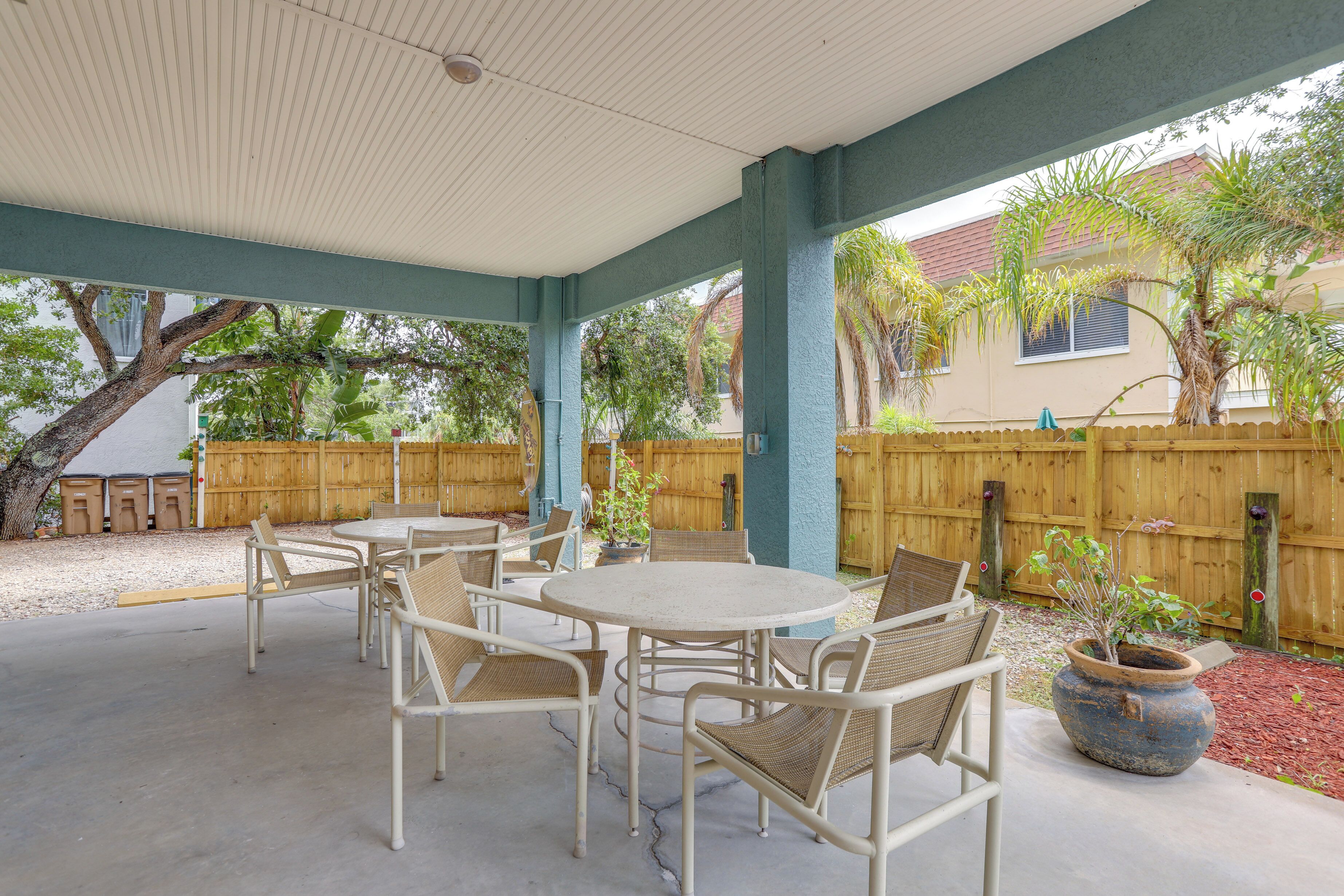 Une terrasse extérieure avec une table ronde et des chaises, un pot de fleurs et une clôture en bois en arrière-plan.