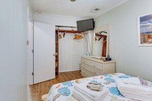 A bedroom with a bed, a dresser, a television mounted on the wall, and a closet with clothes and hangers.