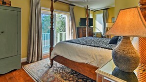 Een slaapkamer met een hemelbed, een plafondventilator, een groot raam met gordijnen, een televisie en een lamp.