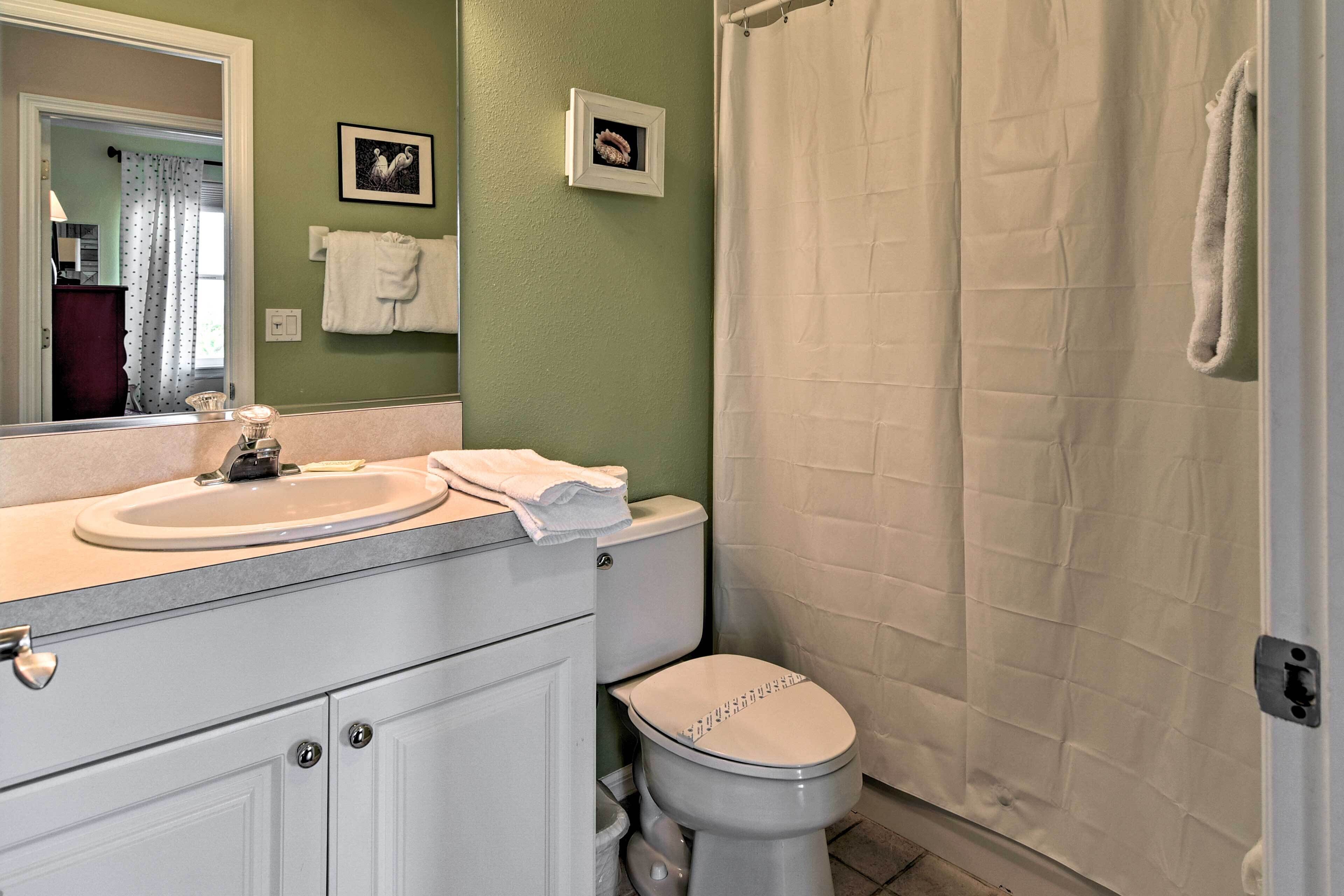 Une salle de bain avec un lavabo blanc, des toilettes et un rideau de douche. Deux tableaux encadrés sont accrochés au mur.