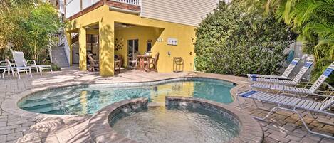 A swimming pool with a hot tub, lounge chairs, and a covered patio area.