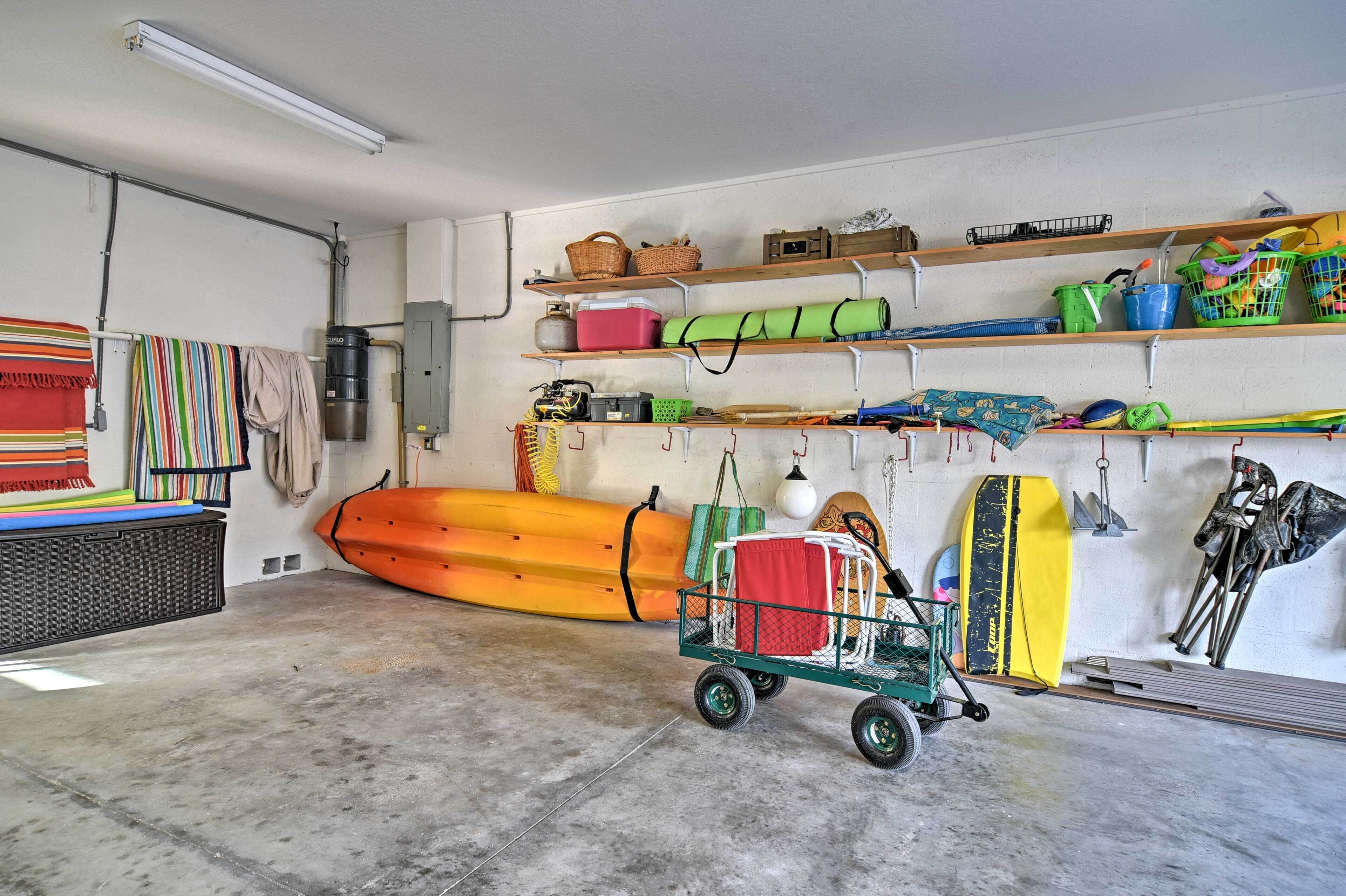 A garage with a concrete floor, shelves with various items, a kayak, and a cart with a life preserver.