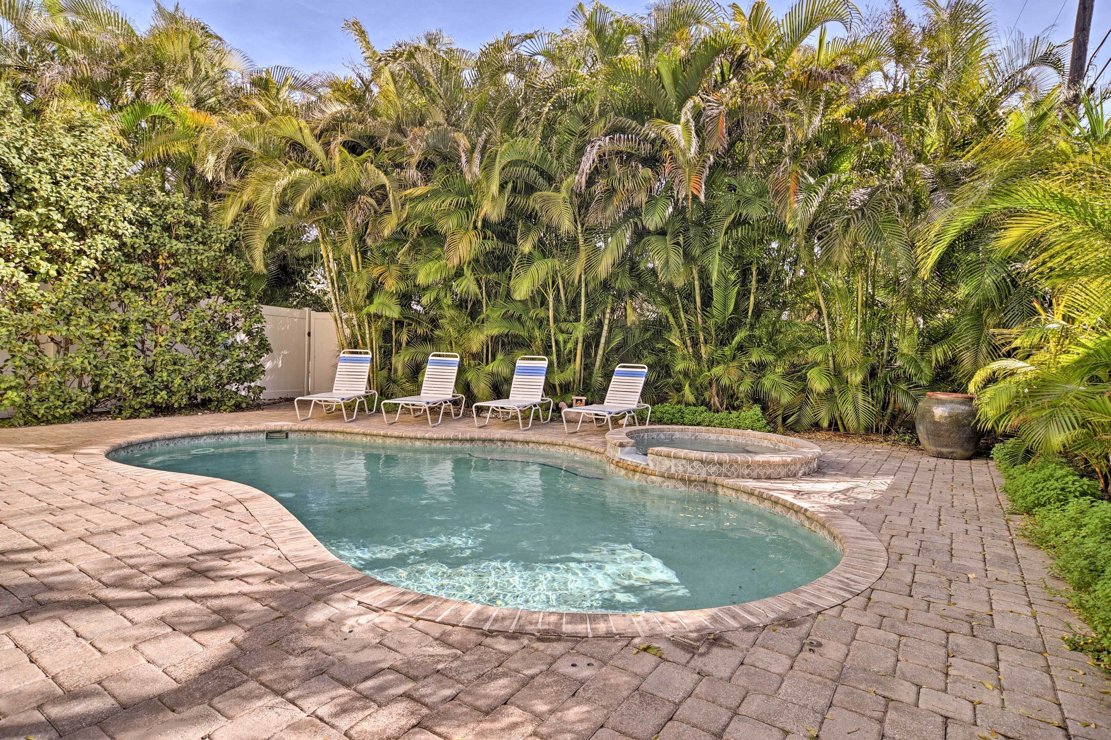A swimming pool with a brick border, surrounded by lush greenery and palm trees.