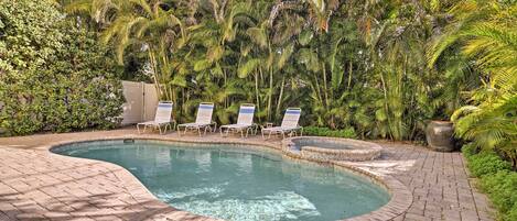 A swimming pool with a brick border, surrounded by lush greenery and palm trees.