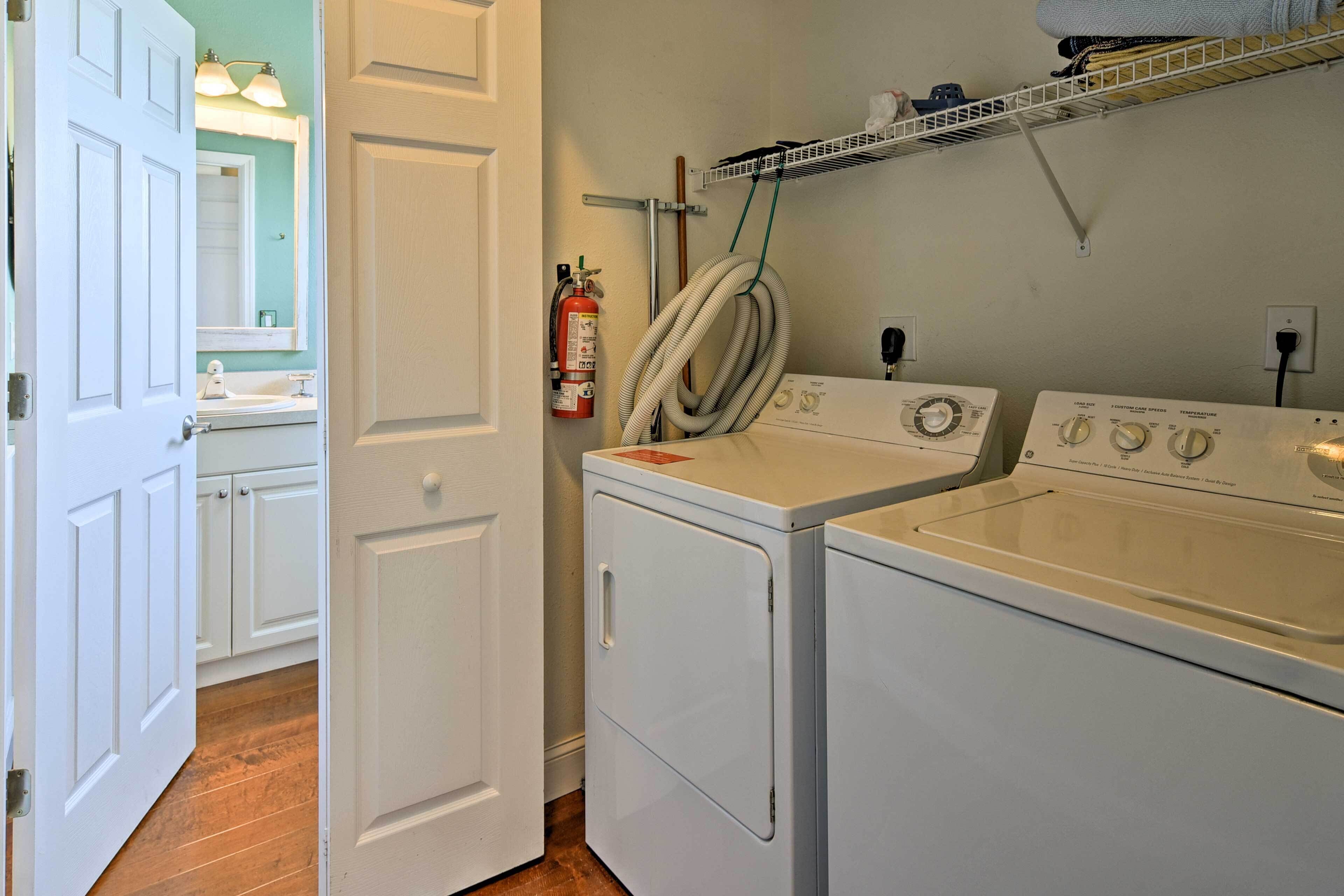 A laundry room with two front-loading washing machines, a fire extinguisher, and a hose.