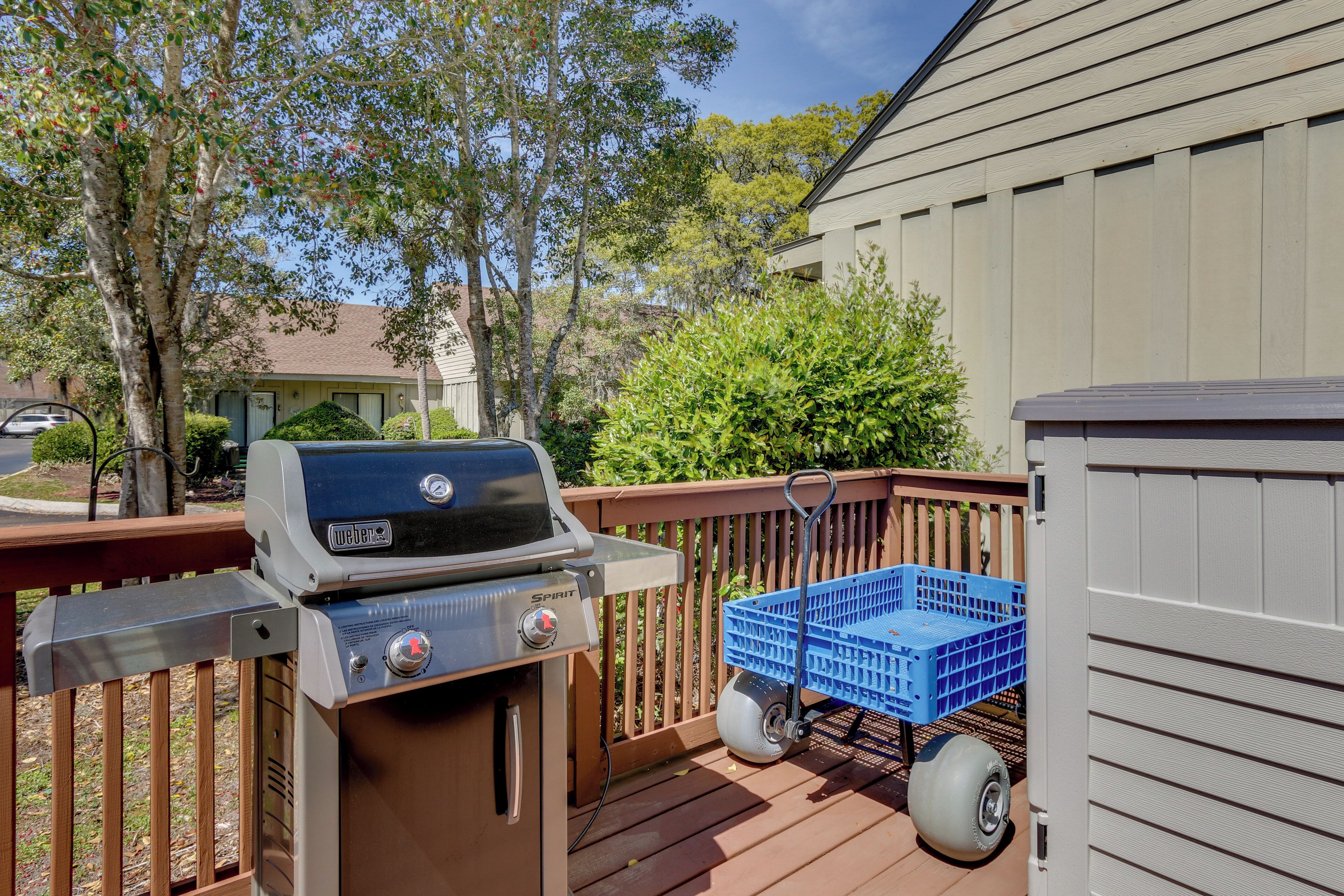 Una parrilla para barbacoa en una terraza de madera con un contenedor azul cercano.