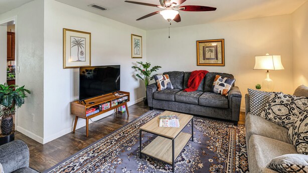A living room with a flat-screen TV, a gray sofa, a coffee table, and a ceiling fan. - Mcgarity Lakehouse: Disney & Universal Day Trip (Deltona)