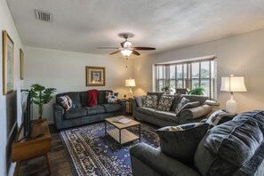 A living room with a ceiling fan, two couches, a coffee table, and a large window with blinds. - Mcgarity Lakehouse: Disney & Universal Day Trip (Deltona)