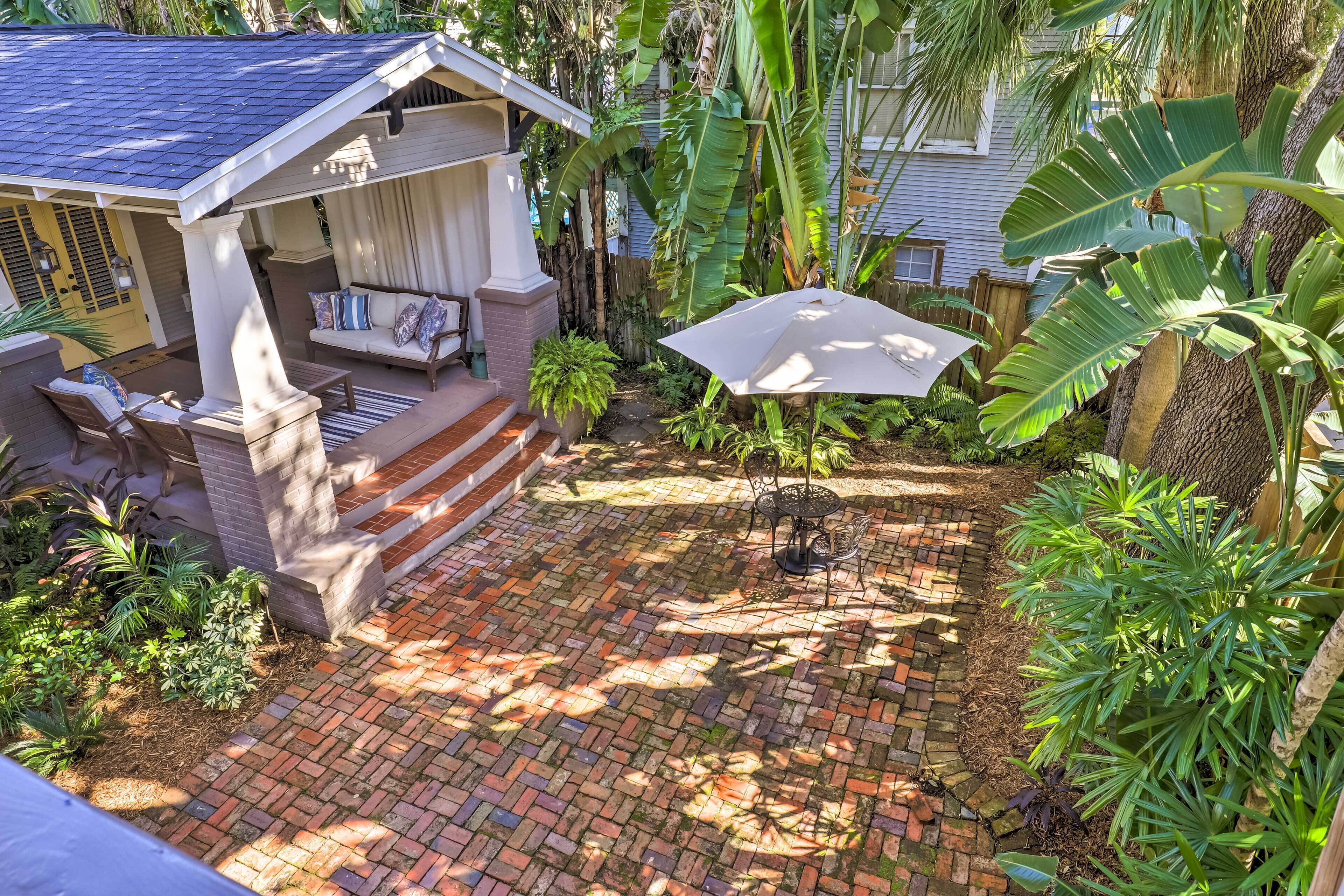 A patio with a brick floor, a covered seating area with a sofa and chairs, and a table with an umbrella.