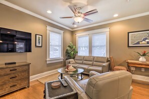 Un salon avec un canapé beige, une table basse en verre, un ventilateur de plafond et un téléviseur fixé au mur.
