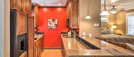 A kitchen with wooden cabinets, a granite countertop, and a red accent wall.
