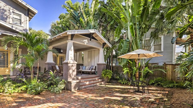 A patio with a covered seating area, brick flooring, and lush tropical plants.