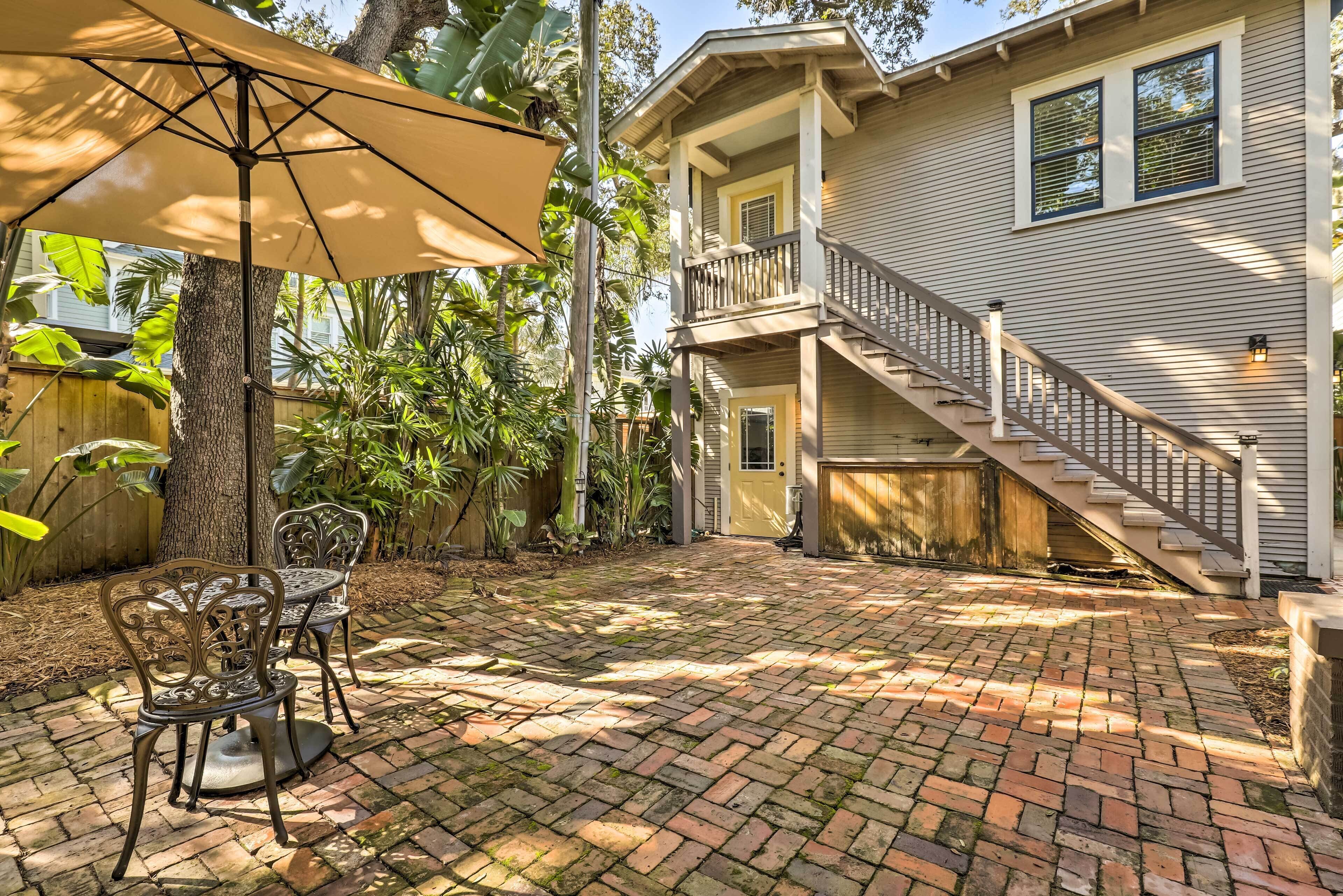 A patio with brick flooring, a table and chairs, and a large umbrella.