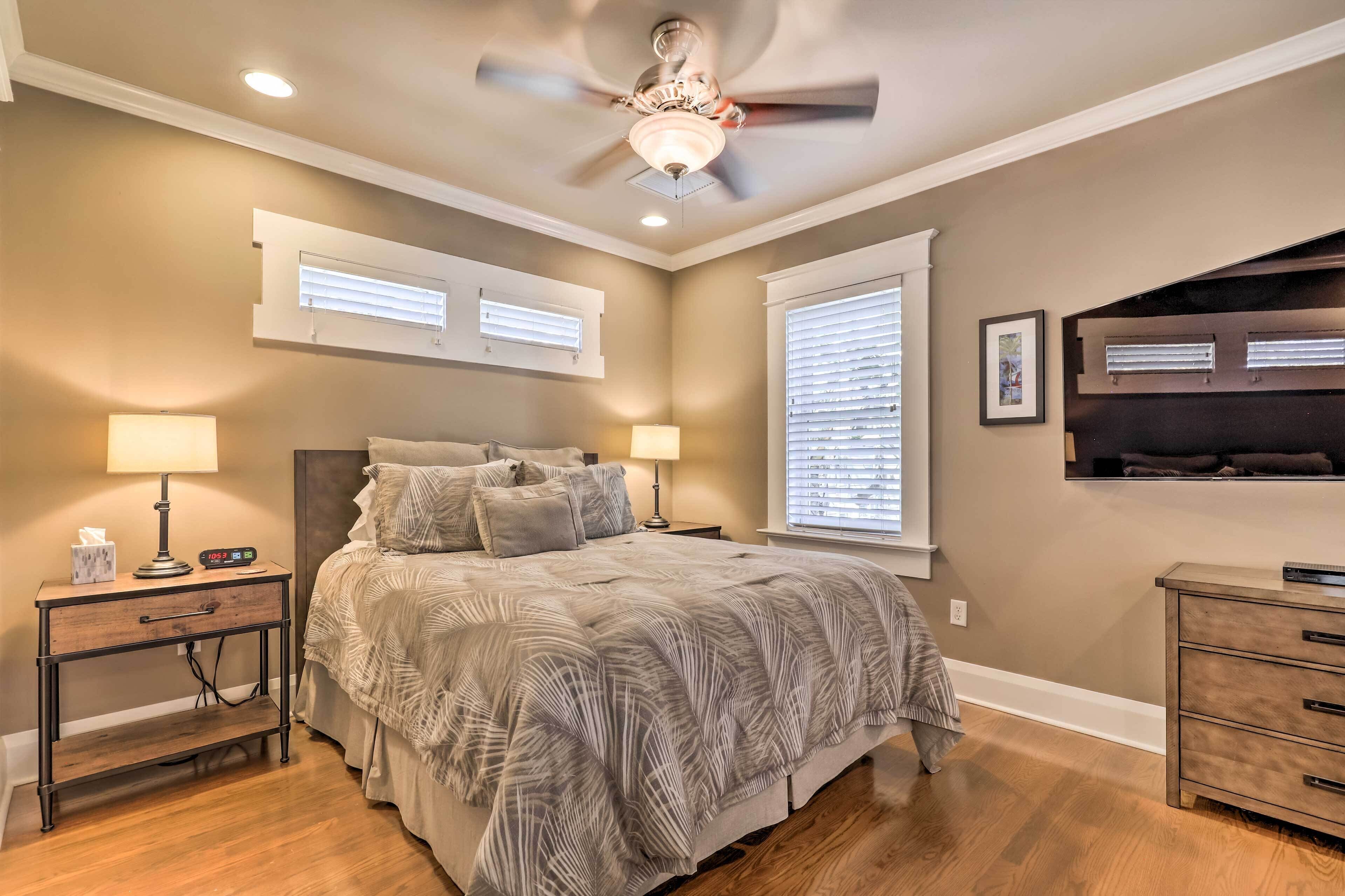 A bedroom with a bed, nightstands, a ceiling fan, and a TV mounted on the wall.