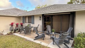 Une maison dotée d’un patio aménagé avec du mobilier d’extérieur, une porte-fenêtre coulissante et un petit jardin avec des plantes en pot.
