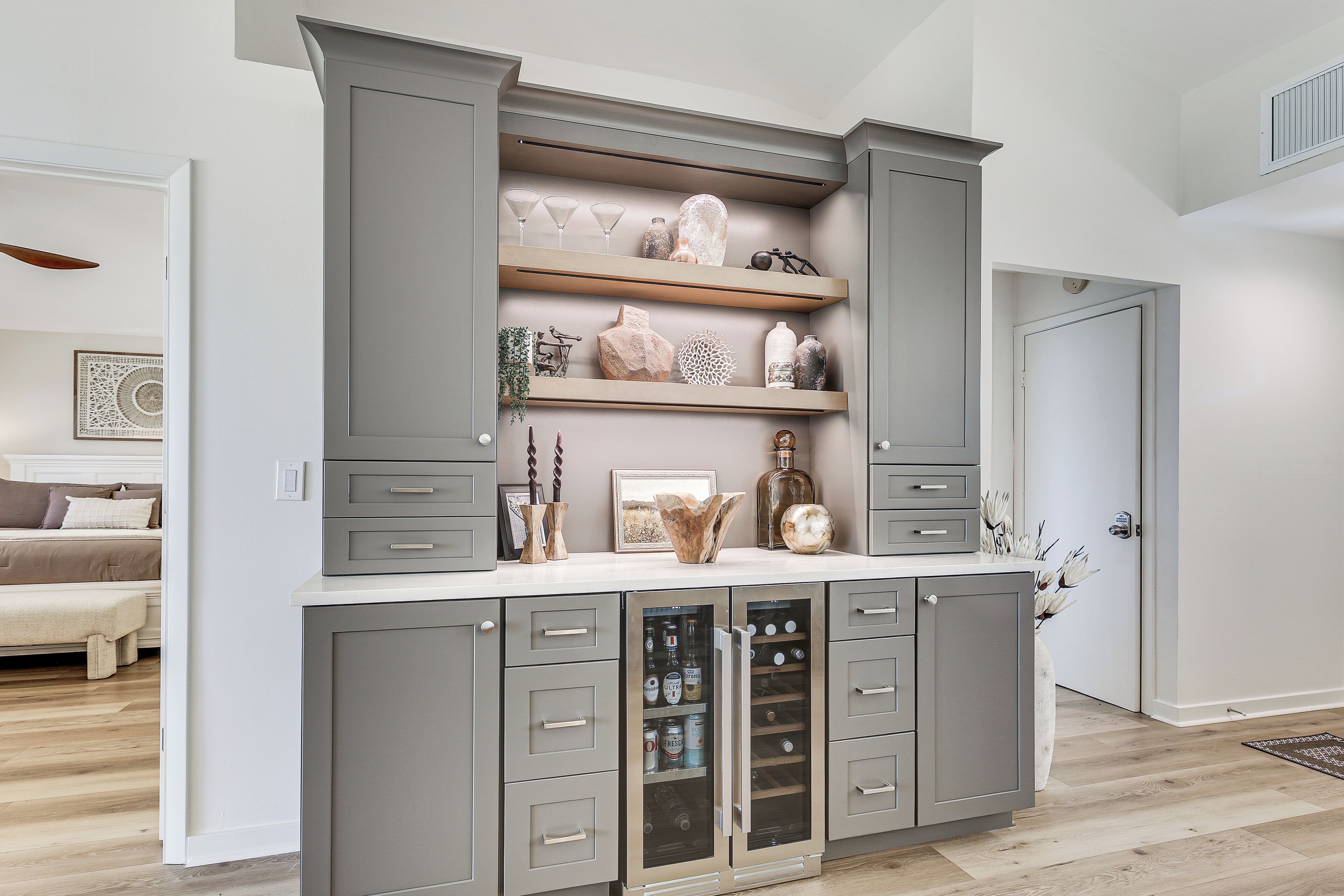 A modern kitchen with grey cabinetry, open shelving with decorative items, and a built-in wine cooler.