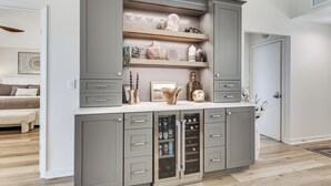 Une cuisine moderne avec des meubles de couleur grise, des étagères ouvertes où sont exposés des objets décoratifs et un réfrigérateur à vin encastré.