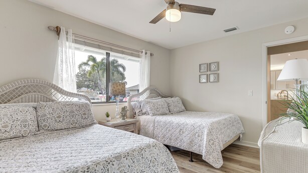 Une chambre avec deux lits, un ventilateur de plafond, une fenêtre avec des rideaux et une porte avec une lampe.